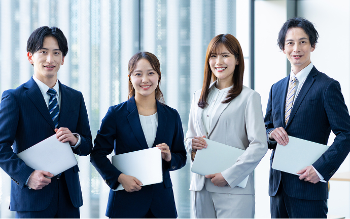 4人の男女のグループがスーツ姿でパソコンを抱えている画像